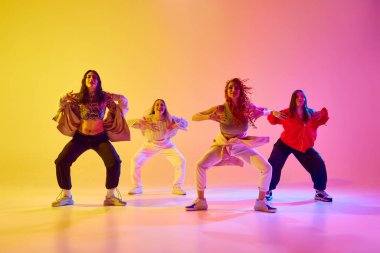 Spor tarzı gündelik giysiler içinde dört sanatsal genç kadın neonlu arka planda serbest dans ediyorlar. Gençlik kavramı, sokak dansı, modern dans, modern dinamik.