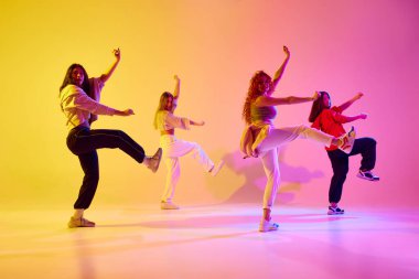 Güzel genç kadınlar, hareketli dansçılar gündelik giysiler içinde neon ışıkta arka planda dans ediyorlar. Gençlik kavramı, sokak dansı, modern dans, modern dinamik.