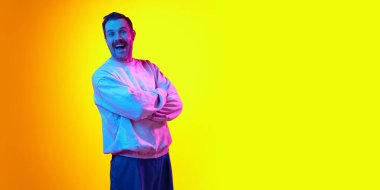 Kolları çapraz duran ve neon ışıklı sarı arka planda gülümseyen mutlu ve heyecanlı tişörtlü adam. Haberler, satışlar. İnsan duyguları kavramı, gündelik moda, yaşam tarzı