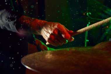 Erkek eline odaklan, renkli ışıklar ve su damlalarıyla siyah arkaplanda davul çalan müzisyen. Canlı bir konser afişi. Müzik kavramı, enstrümanlar, konser, ses, ekipman, festival