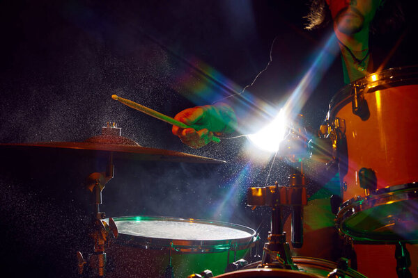 Молодой человек, музыкант играет на барабанах на черном фоне с красочными огнями и каплями воды. Плакат живого концерта. Музыка, инструменты, концерт, звук, оборудование, фестиваль