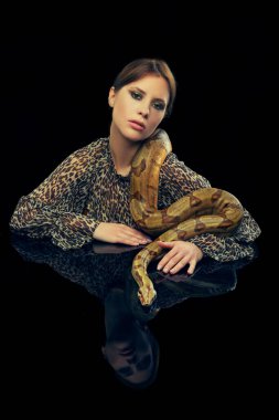 Siyah stüdyo arka planında yılanla poz veren makyajlı genç kadın portresi. Derin duygular. Kadın güzelliği kavramı, hayvan teması, özen, zarafet, moda