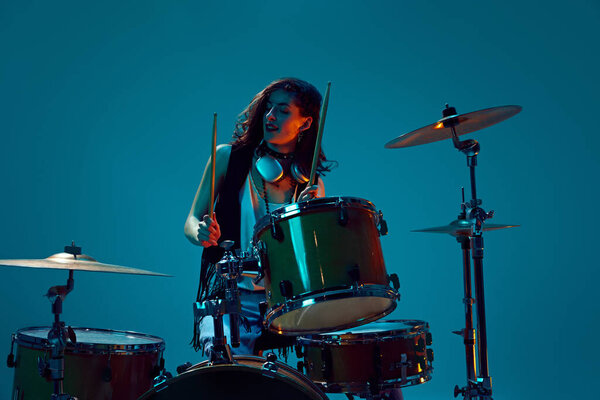 Художественная, выразительная молодая женщина, музыкант, играющий на барабанах на голубом фоне в неоновом свете. Концепция музыки, шоу талантов, перформанс, концерт, фестиваль, инструменты