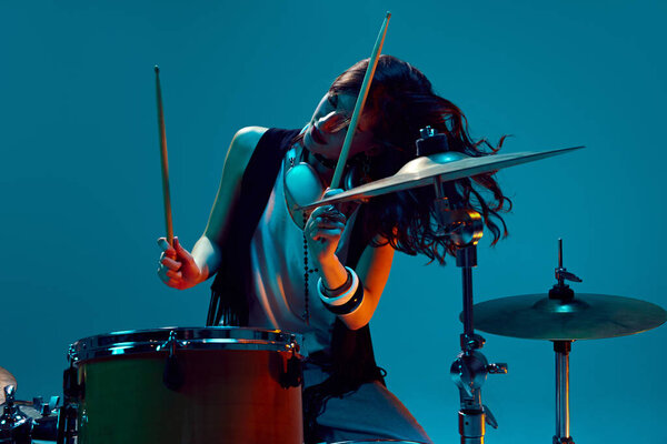 Красивая, энергичная молодая женщина, артистичный музыкант, играющий на барабанах на голубом фоне в неоновом свете. Концепция музыки, шоу талантов, перформанс, концерт, фестиваль, инструменты