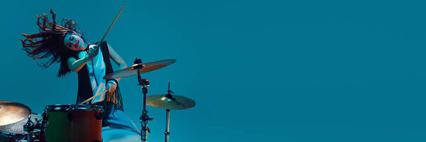 Художественная и энергичная молодая женщина, музыкант играет на барабанах на голубом фоне в неоновом свете. Концепция музыки, шоу талантов, перформанс, концерт, фестиваль, инструменты. Баннер, объявление