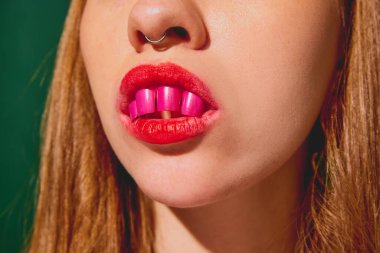 Güzellik salonu için gerçeküstü bir görüntü. Kırpılmış kadın yüzü, içi boyanmış tırnaklarla yeşil arka planda. Pop sanat fotoğrafçılığı, yaratıcılık, tuhaflık, kozmetoloji, sürrealizm kavramı