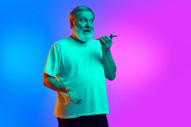 Duygusal sakallı son sınıf öğrencisi cep telefonuyla mavi-mor arka planda neon ışıkta sesli mesaj kaydediyor. İnsan duyguları kavramı, yaşam tarzı, gündelik moda.