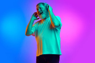 Duygusal, sakallı, son sınıf öğrencisi, gündelik kıyafetler giymiş, kulaklıkla müzik dinleyen neon ışıklarıyla mavi-mor arka planda. İnsan duyguları kavramı, yaşam tarzı, gündelik moda.