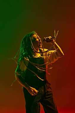Genç bir adam, tutkulu bir müzisyen duygusal olarak neon ışıkta yeşil arkaplanda şarkı söylüyor. Unutulmaz bir gösteri. Müzik, performans, festival, konser kavramı
