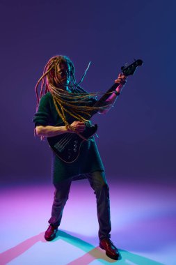 Genç bir adam, müzisyen, rastalı gitar çalan etkileyici gitarist, neon ışıkta koyu mor arka planda solo performans sergiliyor. Müzik, performans, festival, konser kavramı