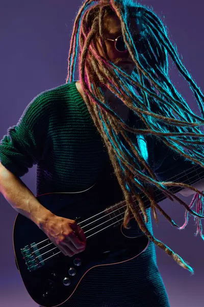 有恐怖头发的时髦男人的肖像 音乐家在霓虹灯下的深紫色背景下弹奏吉他 迷失在音乐中音乐 音乐会的概念 — 图库照片