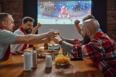 Spor meraklıları, televizyonda online hokey maçı izlemek için evde toplanan arkadaşlar, bira ve atıştırmalıklar heyecanı artırıyor. Spor anlayışı, şampiyonluk, maç, spor fanatikleri, eğlence