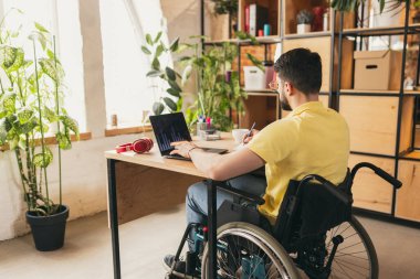 İşadamı, çalışan, tekerlekli sandalyede oturan genç adam, finansal analizler ve bilgi grafikleriyle internette çalışıyor. Sağlık, yaşam tarzı, refah, rahatlık, güçlenme kavramı