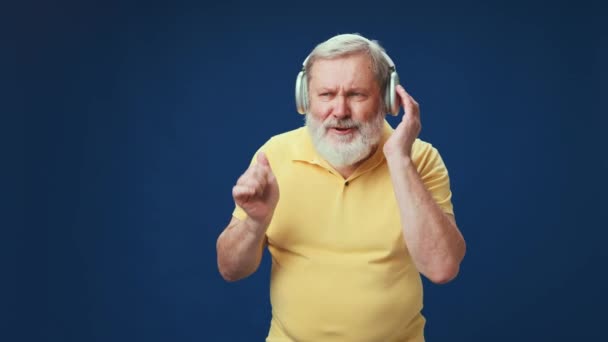 Пожилой Бородатый Мужчина Жёлтом Поло Слушает Музыку Наушниках Фоне Синей — стоковое видео