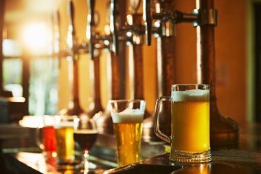 Çeşitli köpüklü biraların olduğu bardaklar ahşap tezgahta bira musluklarının yanında duruyor. Modern bar, bar estetiği. Bira, alkol, bira fabrikası, bar atmosferi, tat.