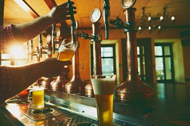 Barmenin yandan görünüşü, bar tezgahında dikilirken erkeklerin bira doldurması. Serin, ferahlatıcı biranın tadını çıkarıyorum. Bira, alkol, bira fabrikası, bar atmosferi, tat.