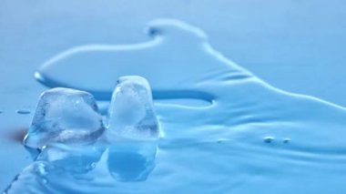 Suyla dolu bardakta eriyen iki buz küpü. Kristal berraklığında damlacıklar. Serinlik ve ferahlık. Ferahlatıcı kavram, ürün estetiği, sağlık, sağlık, susuzluk