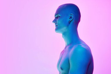 Tişörtsüz, kaslı genç bir adamın yan görüntüsü. Gradyan mavi arka planda, neon ışıkta poz veriyor. Erkek güzelliği, vücut, gençlik, spor, sağlık kavramı