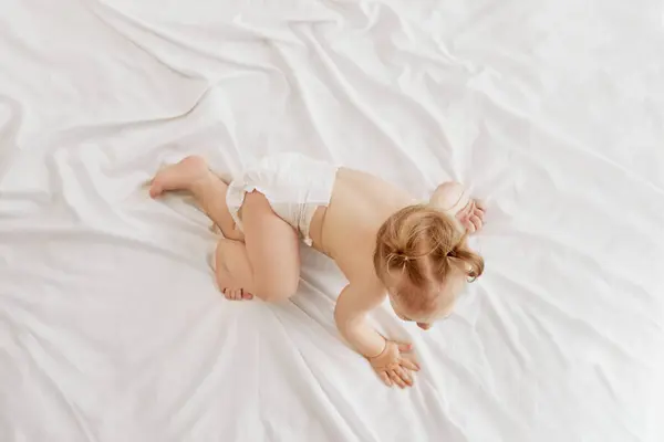 活泼的 微笑的 红头发的小女孩 穿着尿布的幼儿躺在床上 在白色的床单上玩耍 养育子女的概念 — 图库照片