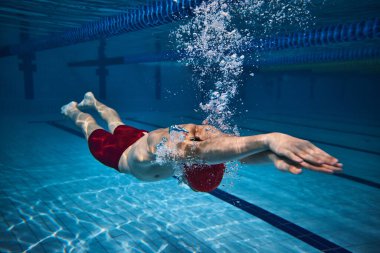 Atletik genç adamın dinamik görüntüsü, suyun altında yüzen yüzücü, yüzme havuzu eğitimi. Baloncuklar, hız. Profesyonel spor, sağlık, dayanıklılık, güç, aktif yaşam tarzı kavramı
