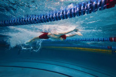 Atletizmin güzelliği iş başında. Genç bir adamın dinamik görüntüsü, hareket halindeki bir sporcu, kapalı havuzda yüzüyor, antrenman yapıyor. Profesyonel spor, sağlık, dayanıklılık, güç, aktif yaşam tarzı kavramı