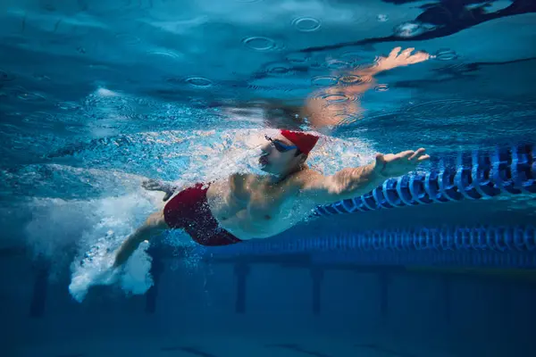 动态形象的小伙子 游泳运动员在红色的帽子和运动的护目镜在游泳池 自由泳 职业运动 积极生活方式的概念 — 图库照片
