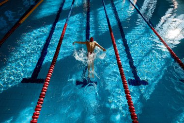 Kaslı, atletik genç bir adam, kırmızı şapkalı yüzücü, hareket halinde, güç gösteriyor, antrenman yapıyor, havuzda yüzüyor. Profesyonel spor, sağlık, dayanıklılık, aktif yaşam tarzı kavramı