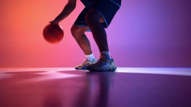 Basketbolcu salya sürme tekniğini gösteriyor, adım adım topun neon ışıkta mor arkaplanda zıplamasını gösteriyor. Profesyonel spor kavramı, rekabet, oyun, eylem