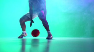 Hareket halindeki erkek basketbolcu, antrenman, salya sürme tekniğinde koordine eden top, neonda duman etkisi olan cyan arka plan. Profesyonel spor kavramı, rekabet, oyun