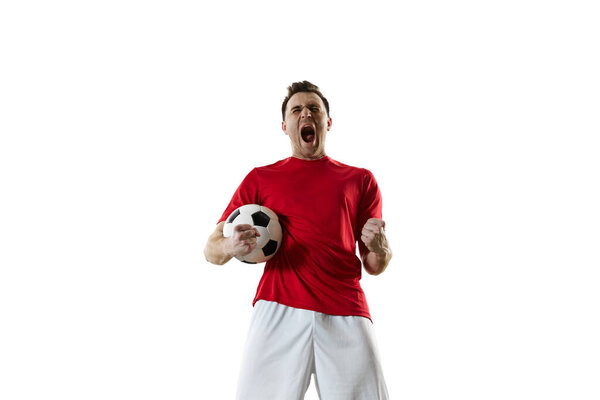Motivated and emotional young man, football player in red uniform standing with ball and shouting isolated on white background. Concept of professional sport, game, competition, tournament, action