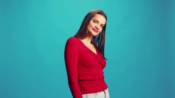 赤い口紅を持つ若い美しい女性 カジュアルな服 笑顔でカメラを見て 青いスタジオの背景にポーズ 人間の感情 ライフスタイルの概念 — ストック動画