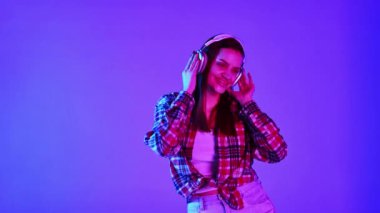 Genç, pozitif, gülümseyen, kulaklıkla müzik dinleyen ve mavi stüdyonun arka planında neon ışığında dans eden mutlu kız. Parti zamanı. İnsan duyguları, yüz ifadesi, yaşam tarzı kavramı