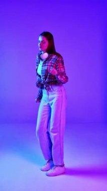 Gündelik giysiler içinde, kulaklıkla müzik dinleyen ve neon ışıklarıyla mavi stüdyoda dans eden genç ve güzel bir kadın. İnsan duyguları, yüz ifadesi, yaşam tarzı kavramı