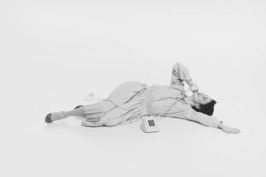 Genç bir kadın yerde uzanıyor ve eski tarz telefonda konuşuyor, gülümsüyor, gülüyor, gevşek sohbet ediyor. Monokrom görüntüsü. Retro ve vintage kavramı, moda, insan duyguları, yaşam tarzı