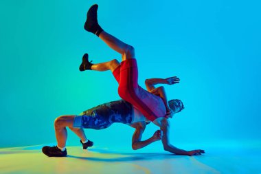 Wrestling male athletes in motion. Young men training, competing for the win against blue background in neon light. Concept of combat sport, martial arts, competition, tournament, athleticism clipart