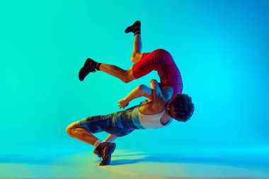 Male wrestlers engage in physical battle, each striving for victory, competing, training against blue background in neon. Concept of combat sport, martial arts, competition, tournament, athleticism clipart