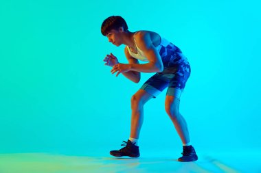 Athletic young man in blue uniform standing in wrestling pose, ready to fight against blue background in neon light. Concept of combat sport, martial arts, competition, tournament, athleticism clipart