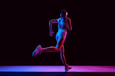 Kaslı, atletik, rahat taytlı, kulaklık takan, siyah arka planda neon giyen genç bir kadın. Aktif ve sağlıklı yaşam tarzı, spor, hobi, motivasyon, dayanıklılık konsepti