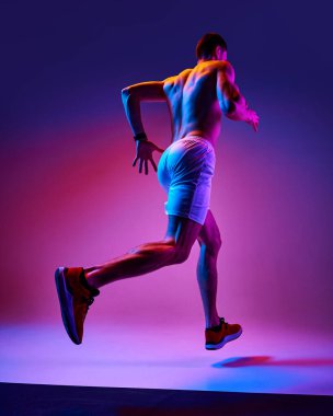 Kaslı, atletik, üstsüz antrenman yapan, neon ışıkta pembe arkaplanda koşan genç adamın alt görüntüsü. Aktif ve sağlıklı yaşam tarzı kavramı, spor, hobi, motivasyon, dayanıklılık