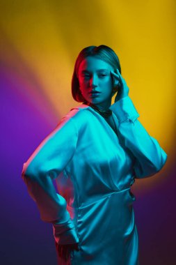 Klasik ve modern estetiğin karışımı. İpek elbise giyen zarif bir genç kadın ve neon ışıkta arka planda bulunan lüks mücevherler. Modern moda kavramı, moda tarzı, güzellik, gençlik