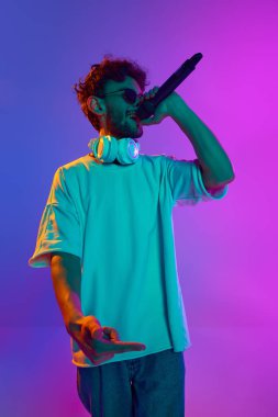 Genç adam, müzisyen sahnede duruyor ve neon ışıkta mavi, cyan arka plana karşı performans sergiliyor. Rap etkinliği. Müzik, performans, festival, konser kavramı