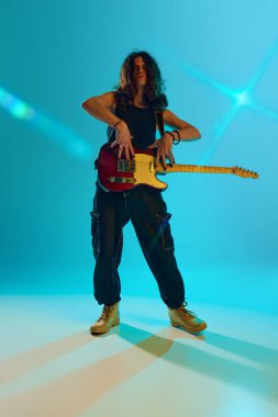 Kararlı bir ifadeyle, genç adam kalbini ve ruhunu performansa döküyor, gitarını mavi, cyan arka planda neon ışıklarıyla çalıyor. Müzik, performans, festival, konser kavramı