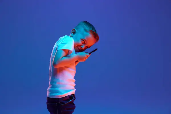 Koulupoika Käyttää Älypuhelinta Yrittää Piilottaa Jotain Sekoitettuun Neonvaloon Sinistä Taustaa — kuvapankkivalokuva