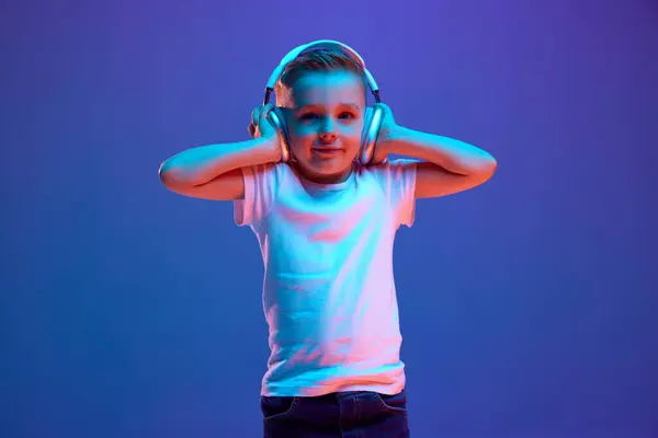 Söpö Pikkupoika Kuuntelee Musiikkia Kuulokkeilla Pitää Sitä Kädestä Sekalaisessa Neonvalossa — kuvapankkivalokuva