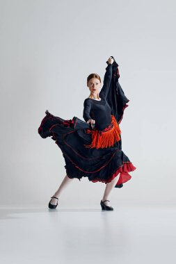 Kırmızı ve siyah elbiseli zarif bir bayanın gri stüdyo arka planına karşı tutkuyla dans ettiği fevkalade flamenko dansı. Hareket sanatı, klasik dans, güzellik, festival kavramı