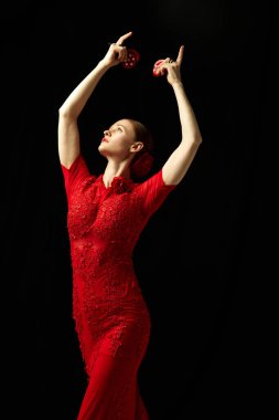 Güzel kırmızı elbiseli zarif bir kadın siyah arka planda kastanyetlerle gösteri yapıyor. İspanyol geleneklerini takip ediyorum. Hareket sanatı, klasik dans, güzellik, festival kavramı