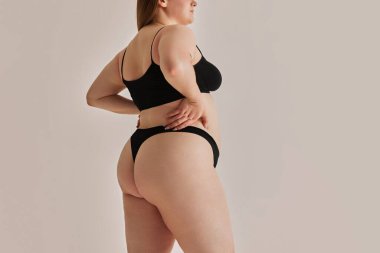 Güzelliğe geniş bir bakış açısı. Büyük beden kadın vücudu, gri stüdyo arka planında iç çamaşırlarıyla poz veren genç bir model. Doğal güzellik kavramı, vücut pozitifliği, özen, kabullenme