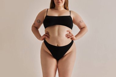 Vücut pozitifliğinin gücünü gösteriyor. Gri stüdyo arka planında, iç çamaşırlı, büyük beden bir kadın cesedi var. Doğal güzellik kavramı, vücut pozitifliği, özen, kabullenme