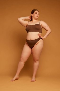 Güzelliğin ve özgüvenin vücut bulmuş hali. Uzun boylu, zarif, iri vücutlu, açık kahverengi arka planda iç çamaşırlarıyla duran güzel bir kız. Doğal güzellik kavramı, vücut pozitifliği, özen.