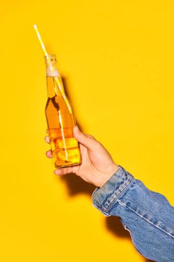 Parlak sarı arka planda samanla limonatalı insan eli şişesi. Alkol ve alkolsüz içecek kavramı, parti, tatil, bar, karışım. Poster. İlan için alanı kopyala